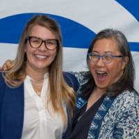 Two faculty members smie and laugh in front of the GVSU backdrop